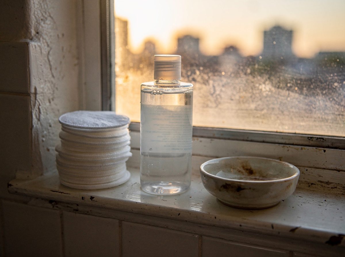 A bottle of micellar water beside cotton pads on a shelf
